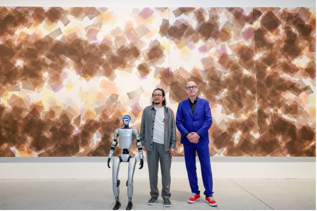 From left to right: the humanoid robot produced by Unitree (Hangzhou) — which took part in the performance How to Explain Painting to a Living Robot; the artist Sang Huoyao; and the exhibition’s curator, Jonas Stampe. The trio is seen during the opening ceremony of Brushstrokes of the Universe at the Museum of Art Pudong, Shanghai, on May 12, 2026. (Courtesy of the artist) © Sang Huoyao Studio